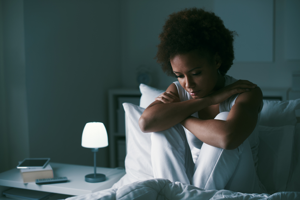 Sad depressed woman sitting in her bed late at night, she is pensive and suffering from insomnia
