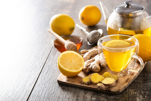 Ginger tea with lemon and honey in crystal glass on wooden table.