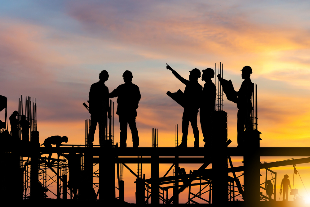 Silhouette of Engineer and worker on building site, construction site at sunset in evening time.