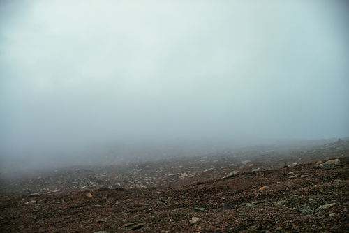 Stone field in dense fog in highlands. Empty stone desert in thick fog. Zero visibility in mountains. Minimalist nature background. Dark atmospheric foggy mountain landscape. Lichens on sharp stones.
