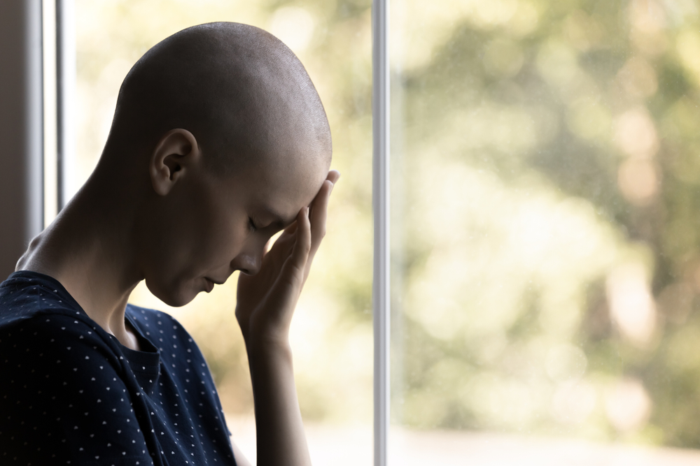Sad exhausted cancer patient suffering prom pain, feeling tired, depressed, disappointed, hopeless. Frustrated hairless girl touching face at window in apathy and despair. Oncology at young age
