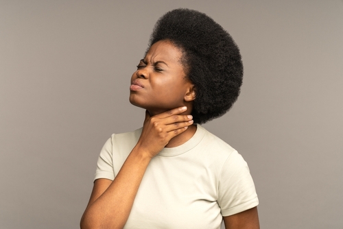 Unhealthy african girl having sore throat, suffering from painful swallowing, strong pain in throat or loss of voice holding neck isolated on studio grey background. Tonsillitis angina thyroid concept