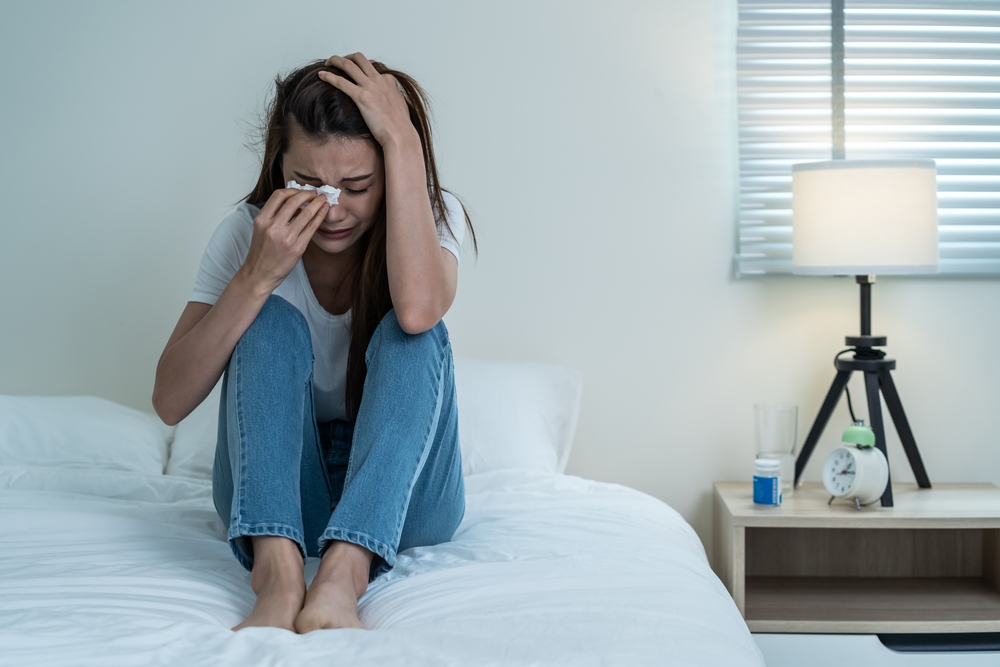 Asian beautiful depression girl crying in tears sit on bed in bedroom. Attractive unhappy young woman feeling sad lonely and upset with life problem and hold tissue on hands in dark night room at home
