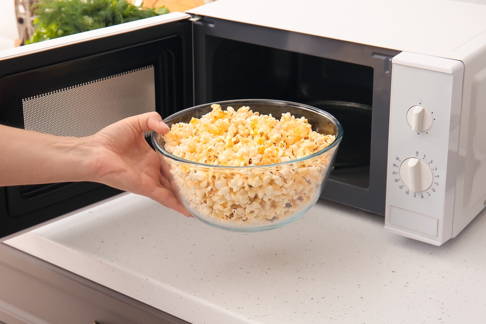 Woman taking bowl of popcorn from microwave oven in kitchen
