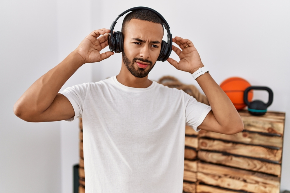 African american man listening to music using headphones at the gym covering ears with fingers with annoyed expression for the noise of loud music. deaf concept.