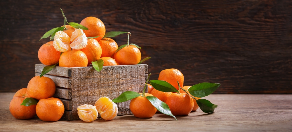 Fresh mandarin oranges fruit or tangerines with leaves in a box on wooden background