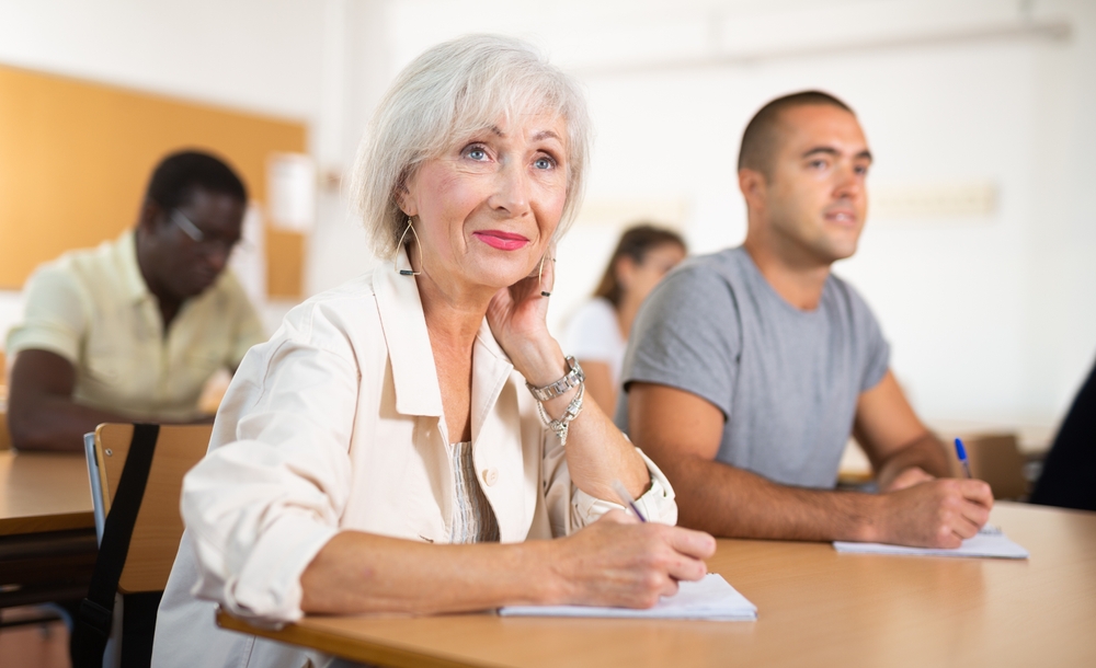 Mature woman learning foreign language with group of younger people in classroom.