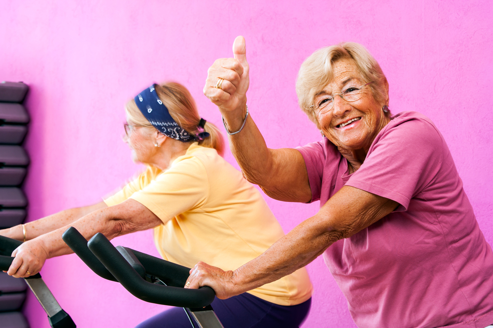 Portrait of happy Senior fitness woman doing thumbs up at spinning session in gym.
