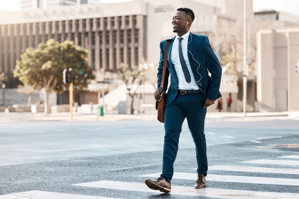 Happy businessman, walking and city to work for travel on street or pedestrian crossing outdoors. Black man on cross road, walk or traveling to business with suit and smile on asphalt in urban town