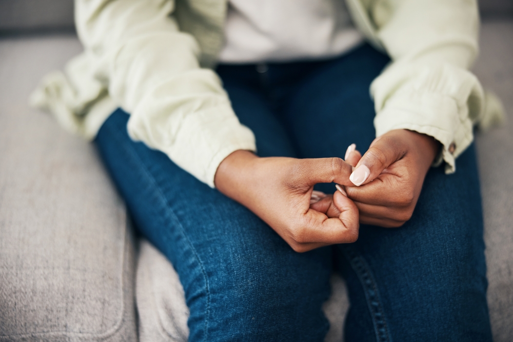 Anxiety, hands and woman on a sofa with stress, worry or mental health crisis in her home. Depression, trauma and zoom on female with bipolar, fear or abuse, danger or nervous nail picking habit
