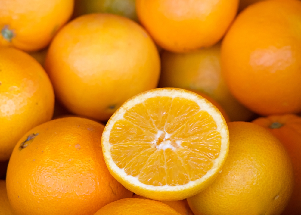 Close up of fresh organic whole navel oranges in a display crate for sale at market. One fruit cut in half for display.