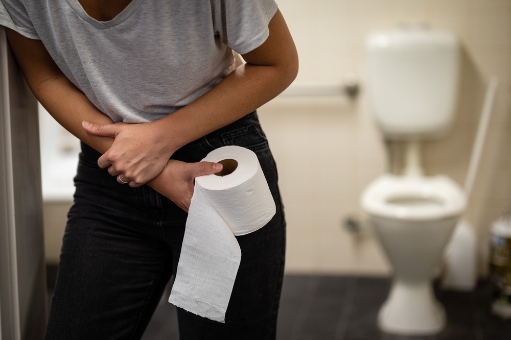 Young female hunched over and holding stomach in pain and discomfort. Hands on abdomen, needs or using toilet. Inflammation, constipation, PCOS, menstruation, or abdominal pains. Close up photograph.

