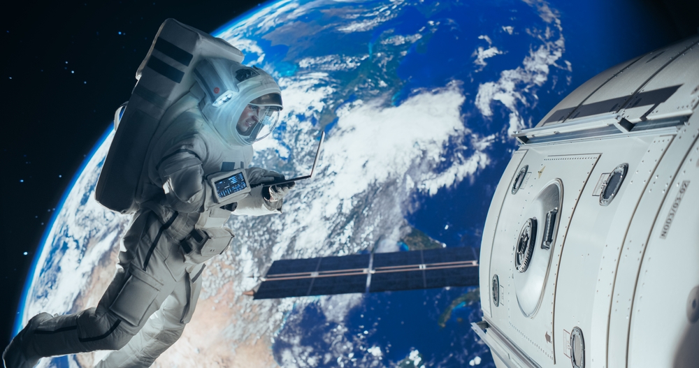 Young Astronaut Floating in Space in Zero Gravity. Spaceman Using Laptop Computer in Open Space Outside an Orbiting Spacecraft, Browsing Instruction Manuals for Maintenance Work on a Satellite