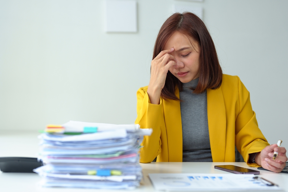 Businesswoman who is tired, sleepy and bored from sitting at a desk for a long time and has office syndrome Asian businesswoman with a headache Stressed with piles of paperwork on your desk.