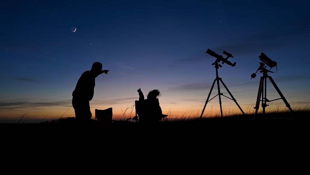 People enjoying watching and stargazing with astronomy telescopes outdoors in nature, observing planets, Moon and other celestial objects.
