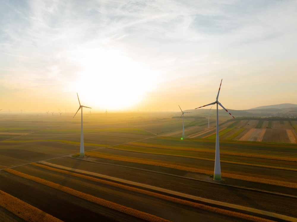Wind turbines harnessing wind power during sunrise, set in an expansive agricultural landscape. Perfect for promoting clean energy and sustainability
