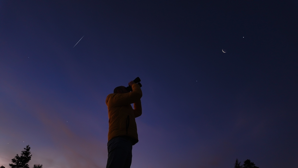 Amateur astronomer looking at the evening skies, observing planets, stars, Moon and other celestial objects with binoculars.
