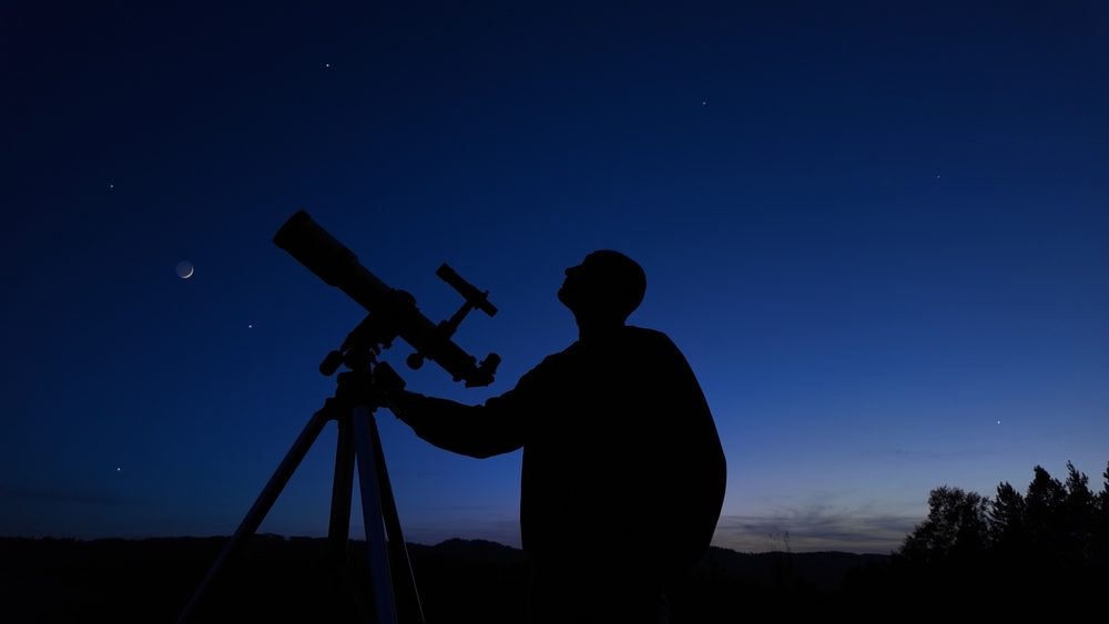 Amateur astronomer looking at the evening skies, observing planets, stars, Moon and other celestial objects with a telescope.