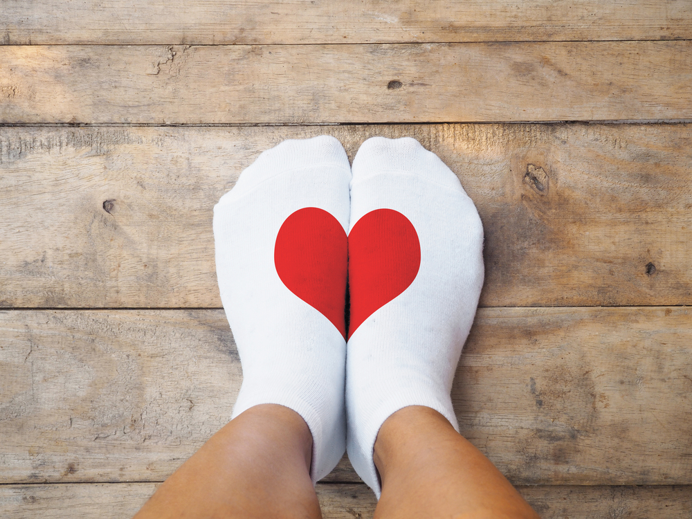 Selfie feet wearing yellow socks with red heart shape on wooden floor background. Love self concept.