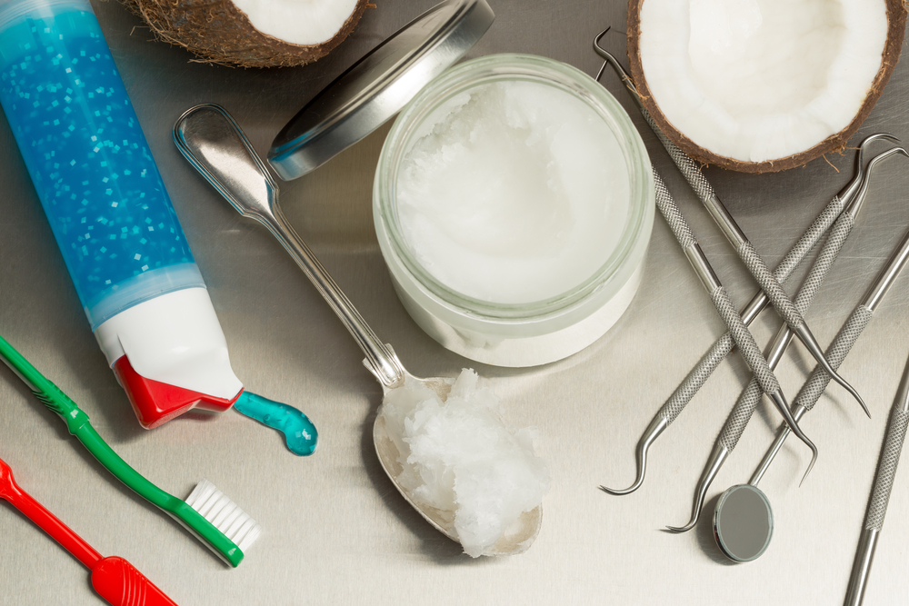Selection of dentists tools on a stainless steel background with coconut oil, toothpaste, toothbrush and floss. Heaped dessert with cocunut oil by jar.