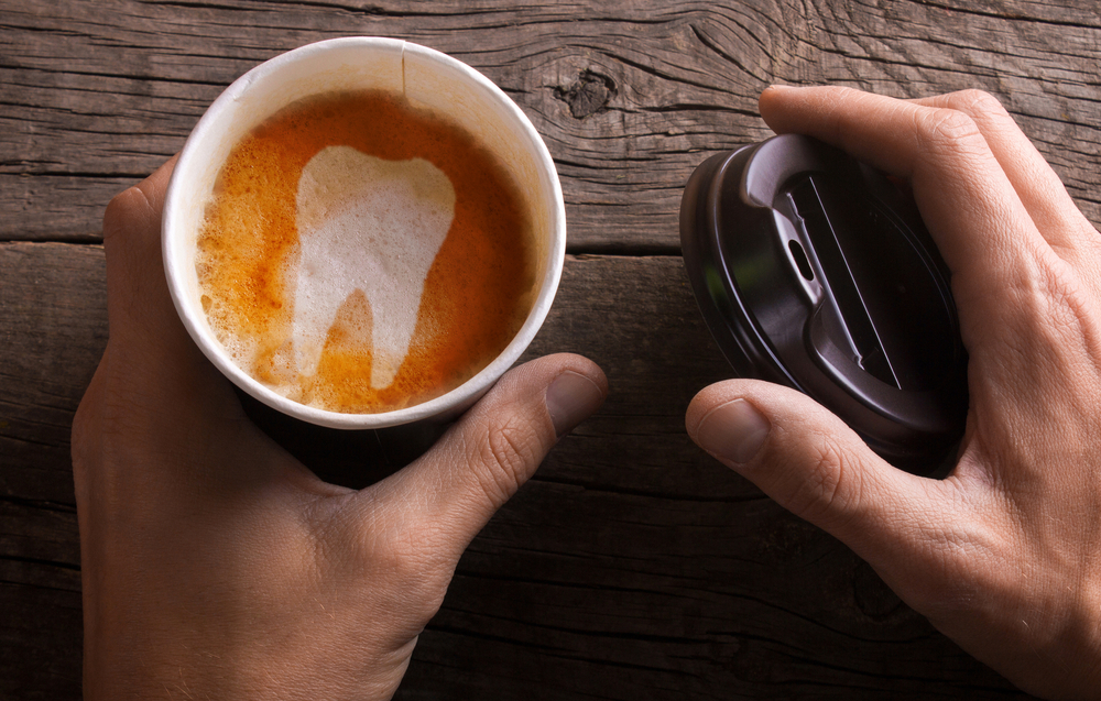 Paper cup of coffee is held by a man in his hand. Coffee makes teeth yellow and sick.