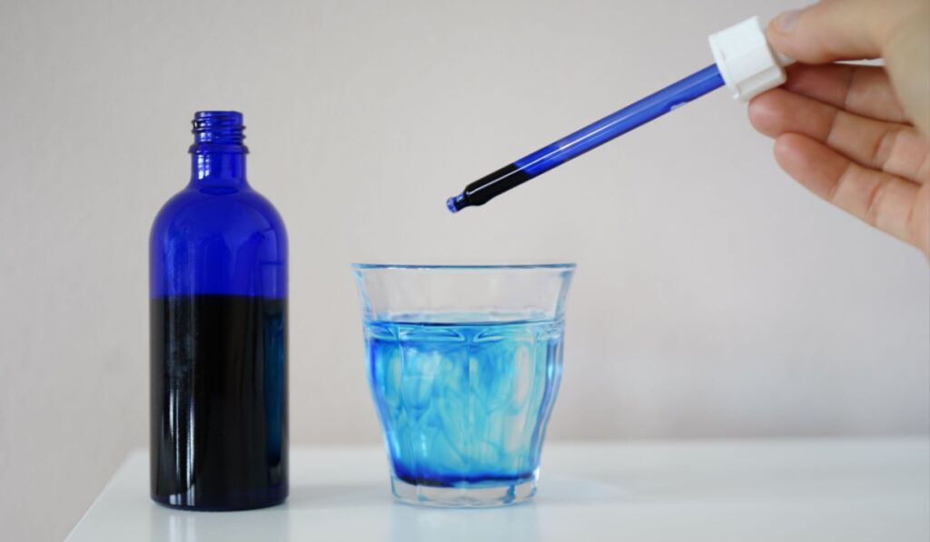 image showing a bottle filled with methylene blue near a glass with water and methylene blue and a pipette