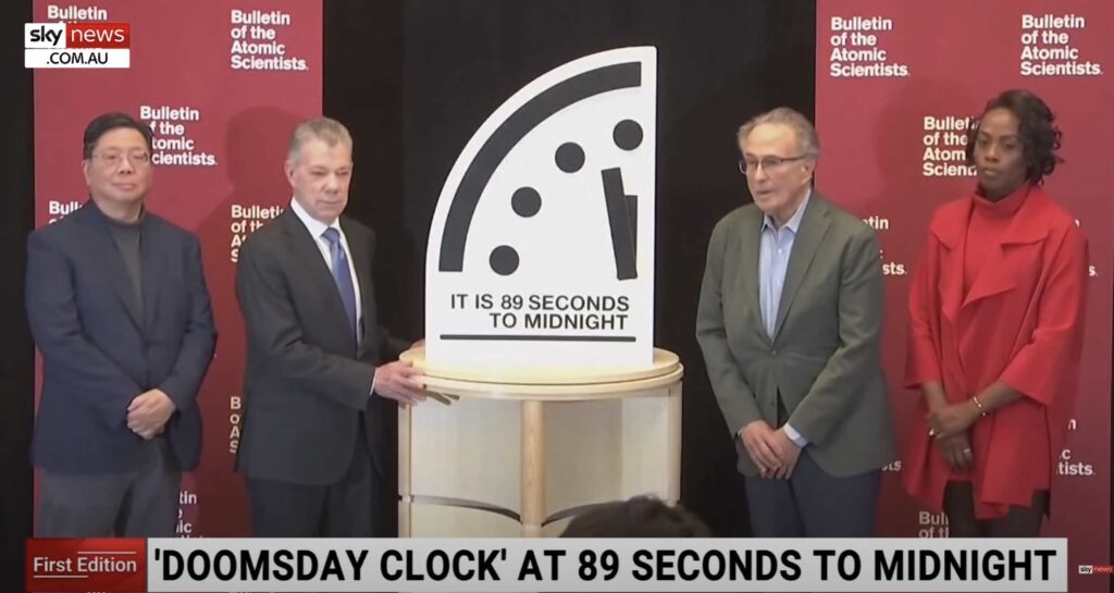 Screen shot of scientists standing beside a representation of the 2025 Doomsday clock being set to 89 seconds to midnight 