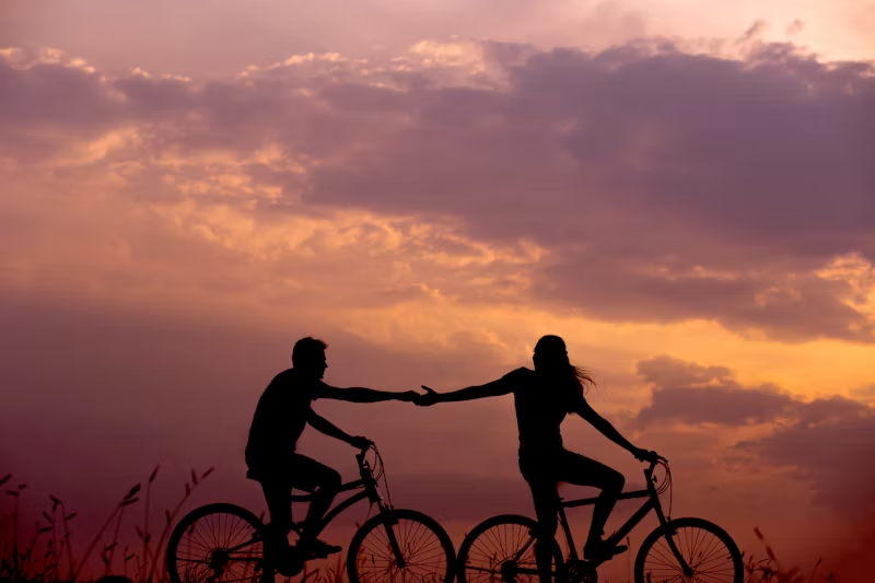 silhouette of two people on a bike holding hands