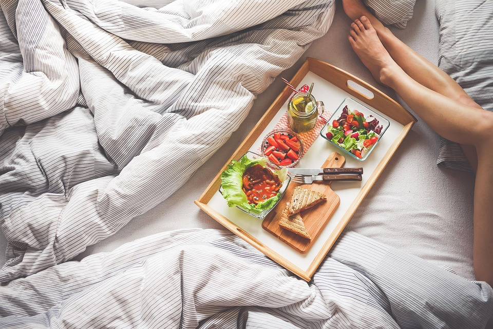 A woman's legs are seen on a bed, next to a tray filled with food