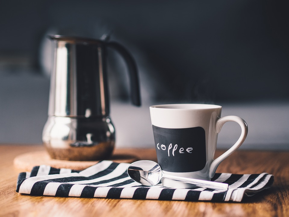 A coffee mug and spoon resting on a table, complemented by a neatly arranged striped napkin.