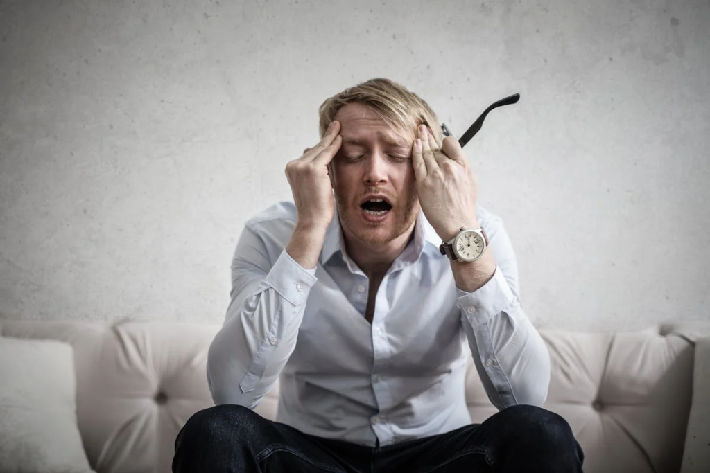 A man sits on a couch, his head resting in his hands, conveying a sense of distress or deep contemplation.