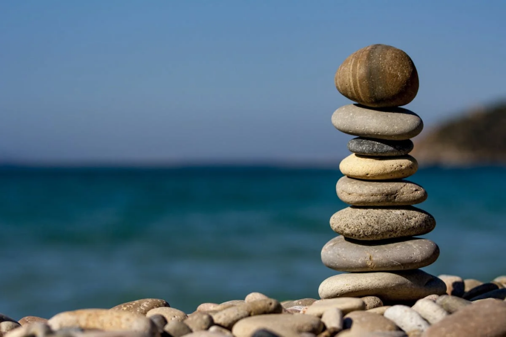 A carefully balanced stack of stones resting on a sandy beach, with gentle waves lapping in the background.