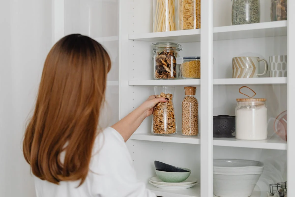 A woman examines a decluttered shelf filled with various food items in a well-organized pantry.
