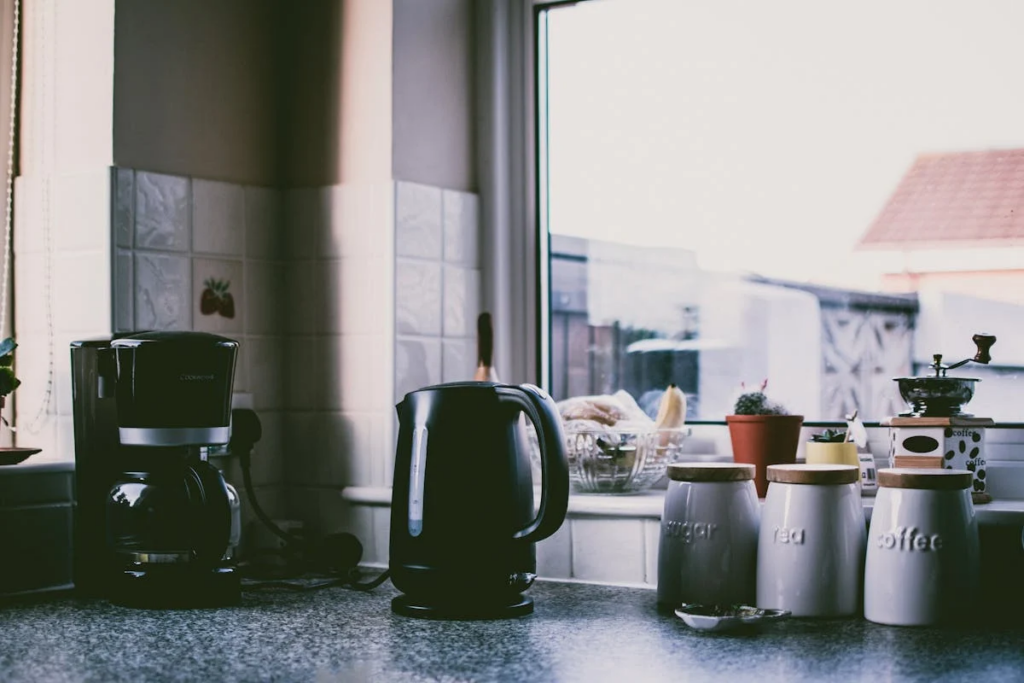 A kitchen counter featuring a coffee maker, pots, pans, and a window, serving as a coffee and tea station.