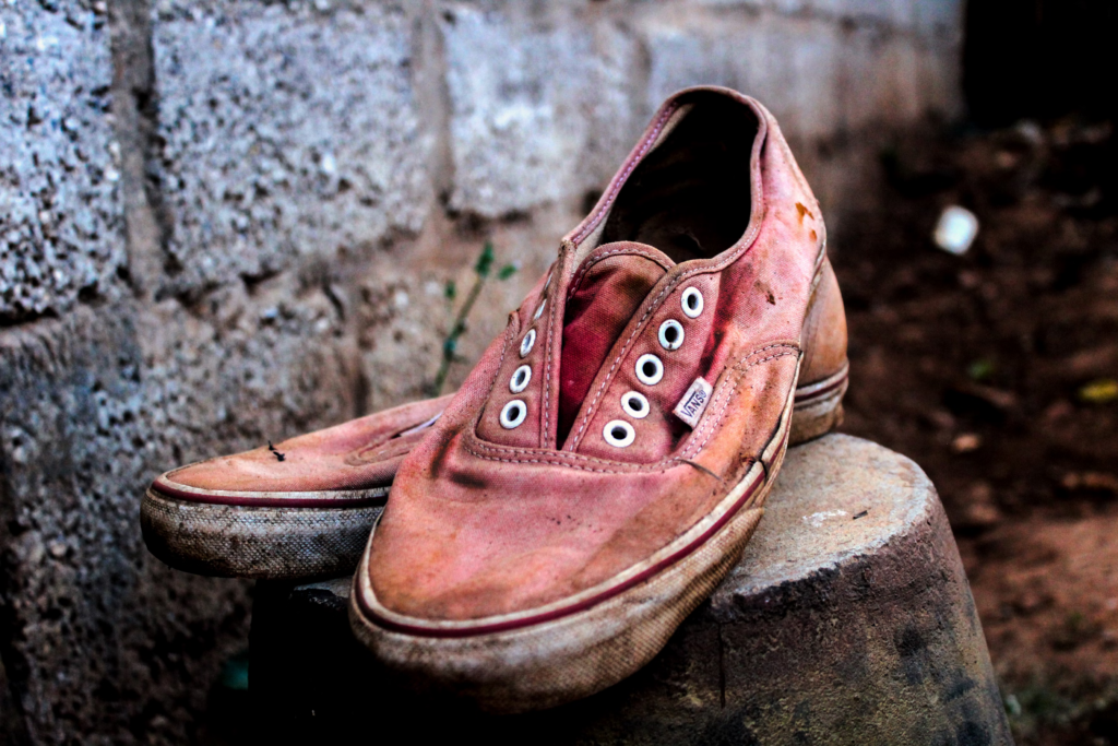 A pair of dirty, worn old shoes resting on a wooden stool, showcasing their age and use.