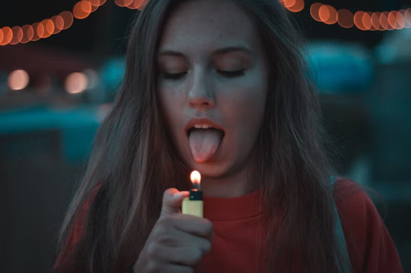 young woman lighting a fire under her tongue