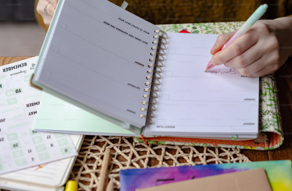 A woman writes in her planner while seated at a wooden table, surrounded by a calm and organized workspace.