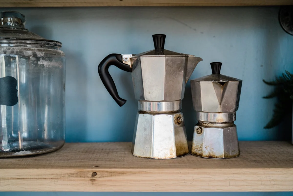 Two coffee pots and a jar arranged neatly on a wooden shelf, showcasing a cozy kitchen aesthetic.