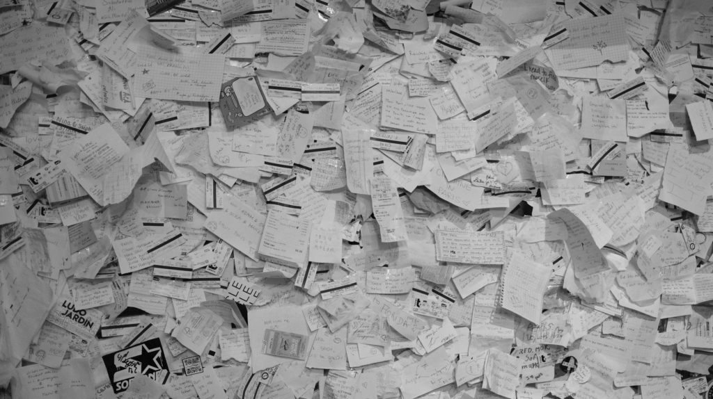 A black and white image depicting a wall entirely covered with various sheets of paper.