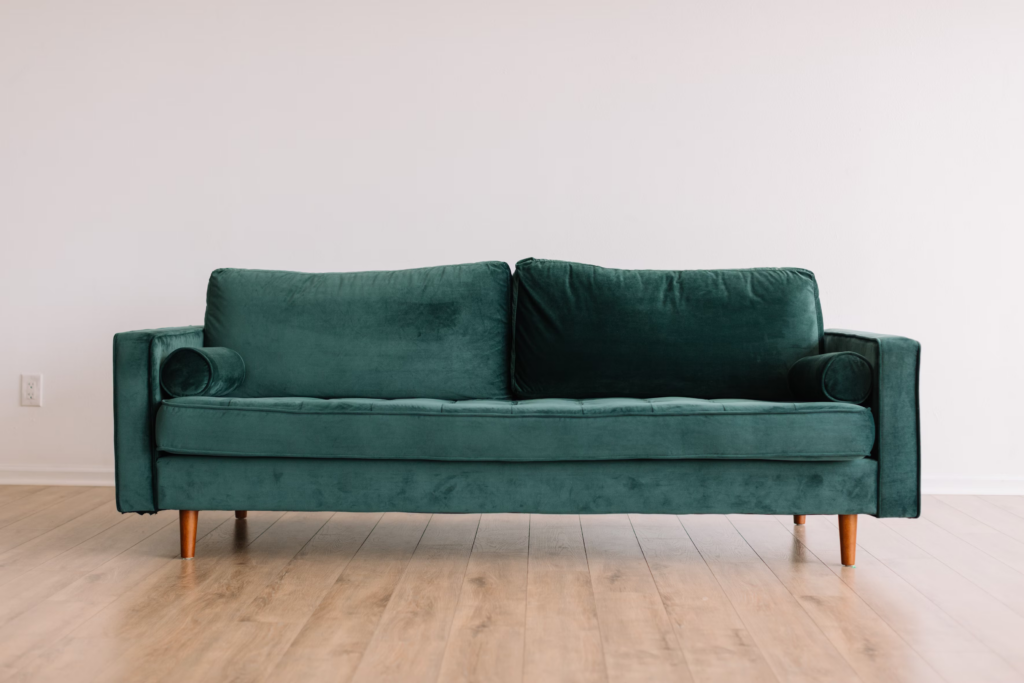 A green velvet couch positioned elegantly against a pristine white wall, creating a striking contrast in the room.