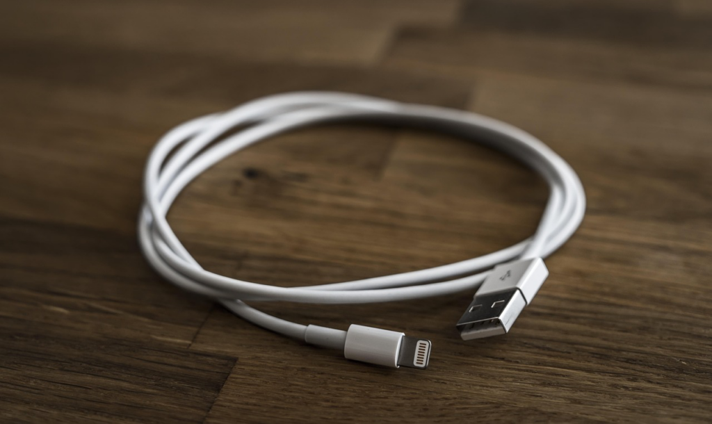 A decluttered white USB cable lightning cable on a wooden table.