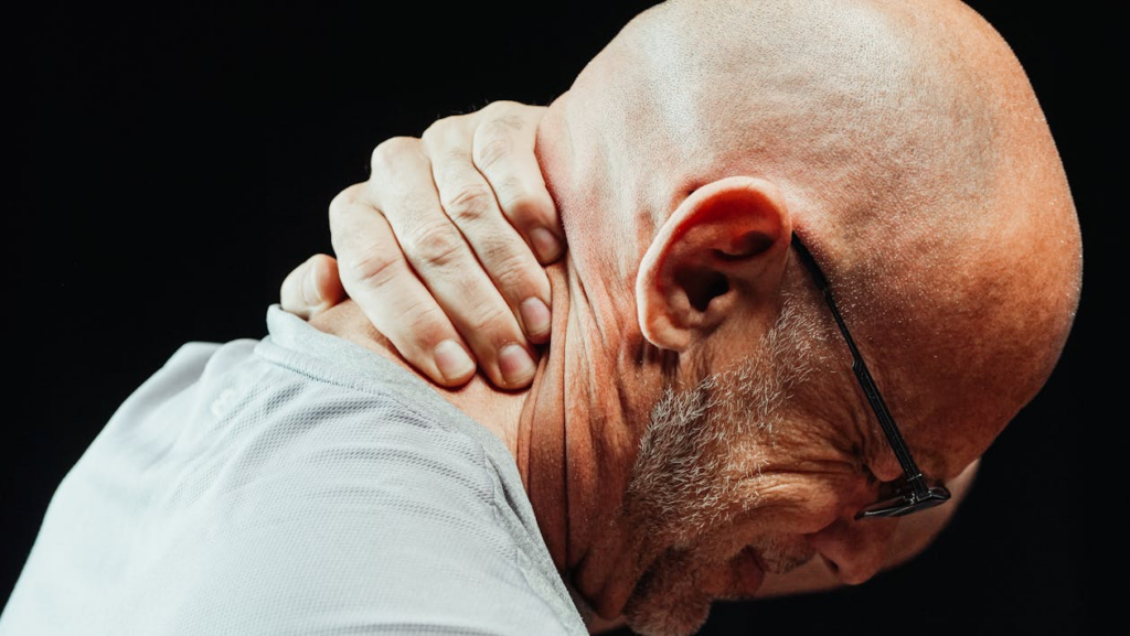 A bald man experiences neck pain, reflecting the connection between physical discomfort and emotional distress.