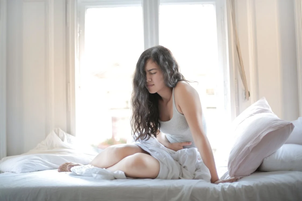 A woman sits on a bed, clutching her stomach in pain, illustrating the connection between gut health and mental well-being.