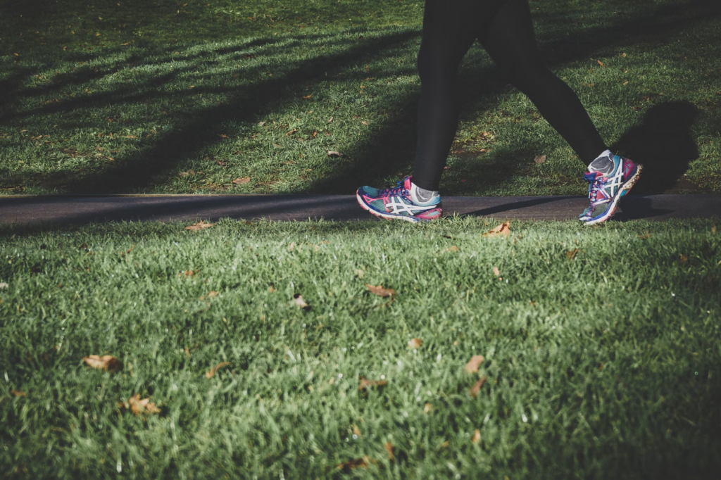 A person walks along a grassy path, embodying the healing power of movement through their steps on the earth.