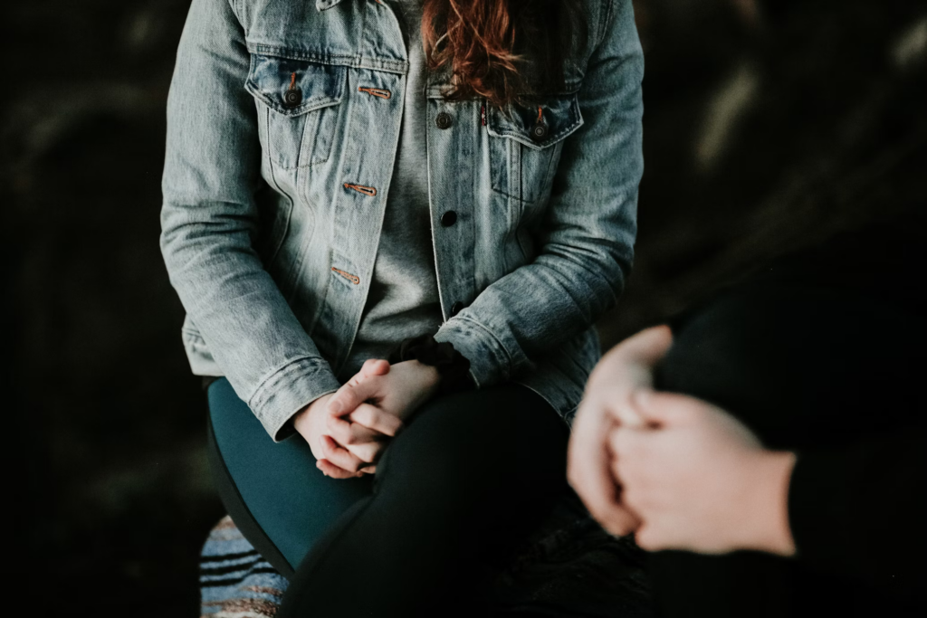 A woman sitting with her hands folded, reflecting during a therapy session.
