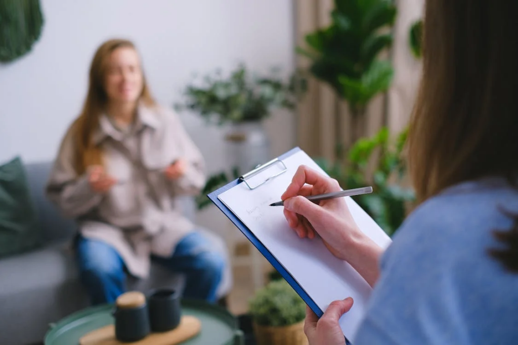 A woman sits on a couch, discussing her IVF journey with a therapist who is taking notes on a clipboard.