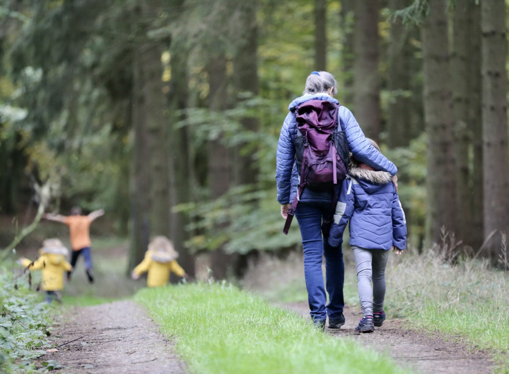A woman and two children stroll through a lush forest, enjoying a day outdoors together.