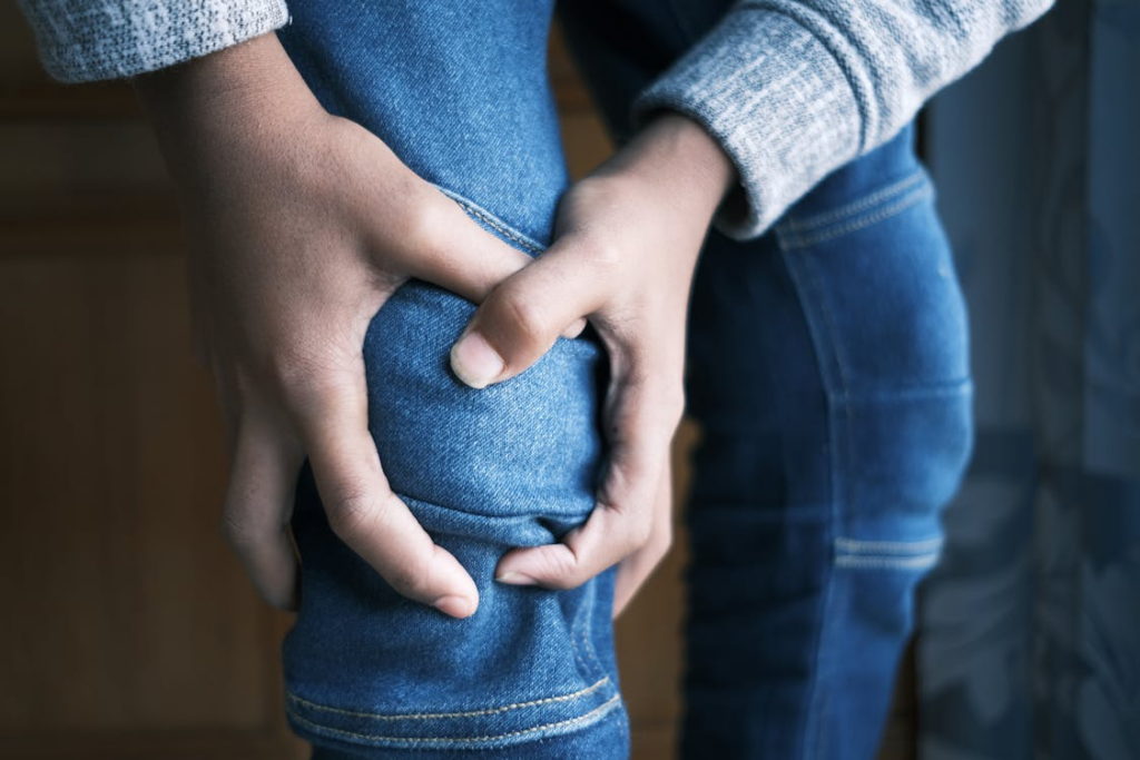 A person grimacing while holding their knee, showing signs of pain from Peripheral Artery Disease symptoms.