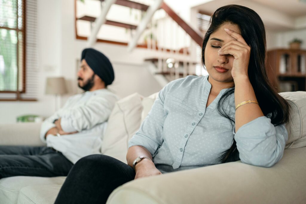 In a living room, a man and woman sit on a couch, both appearing distressed and engaged in a serious conversation.