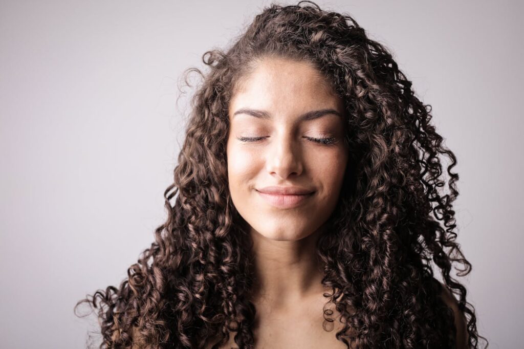 Portrait Photo of Smiling Woman with Brown Curly Hair with Her Eyes Closed

